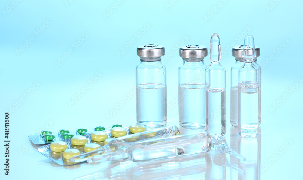 Syringe with medical ampoules and tablets on blue background Syringe with medical ampoules and tablets on blue background