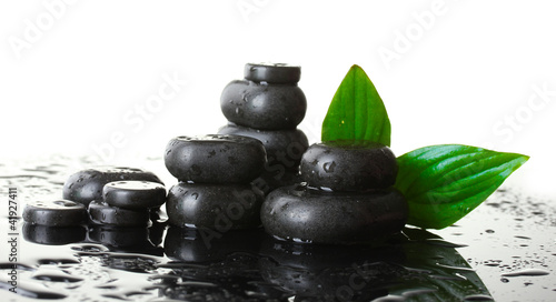 Spa stones with drops and green leaves on white background