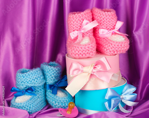 pink and blue baby boots, pacifier and gifts on silk background.
