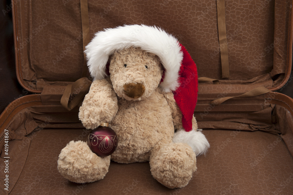 teddy with xmas hat and ornament seated in open suitcase