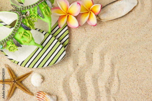 Green Sandals, seashells, starfish and frangipani on sand.