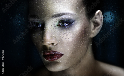 Beauty portrait of gorgeous woman behind rainy glass