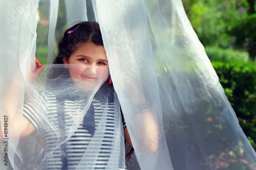 cute little girl hiding face behind transparent tissue in summer