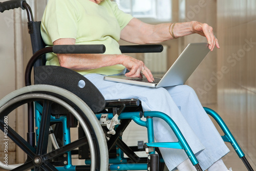 Senior Woman Sitting In Wheelchair Using Laptop