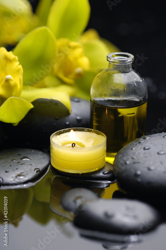 burning candle and yellow orchid  with massage oil on pebbles