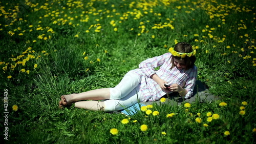 Teenager girl lying on meadow full of sow-thistle with cellphone