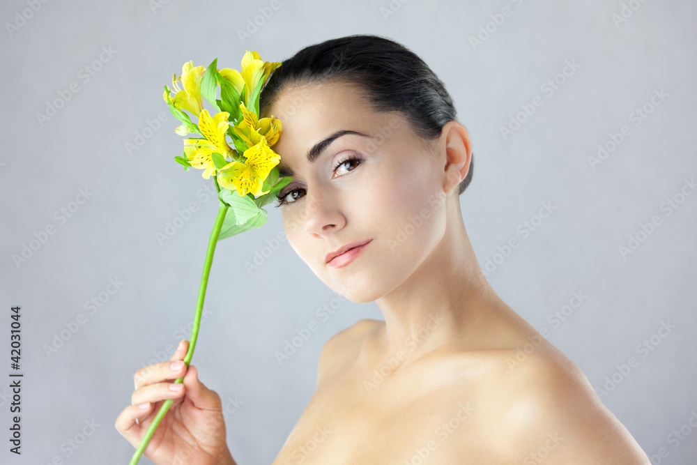 Obraz premium Twarz pięknej kobiety z uśmiechem i kwiatem w dłoni