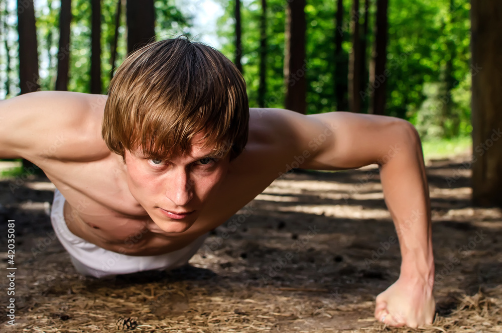 Attractive man doing a push up in forest Attractive man doing a push up in forest