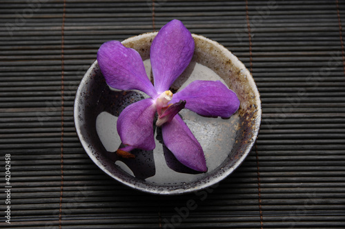 Purple orchids in wooden bowl on bamboo stick straw mat