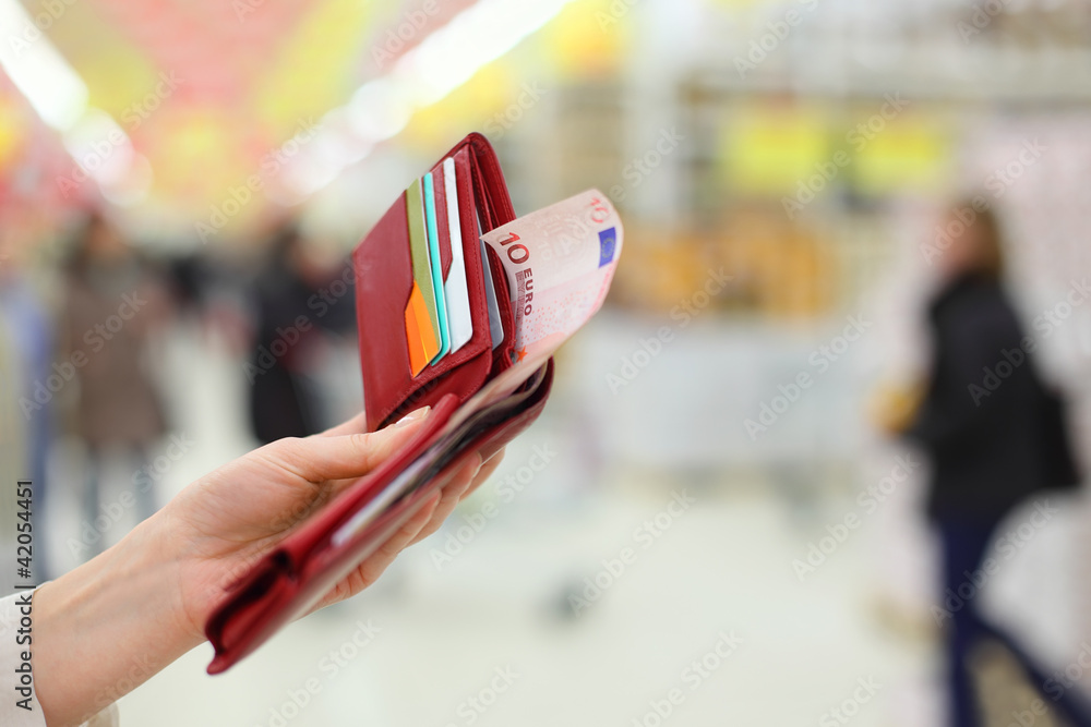 Woman hand keep red purse with money and credit cards in store; Woman hand keep red purse with money and credit cards in store;