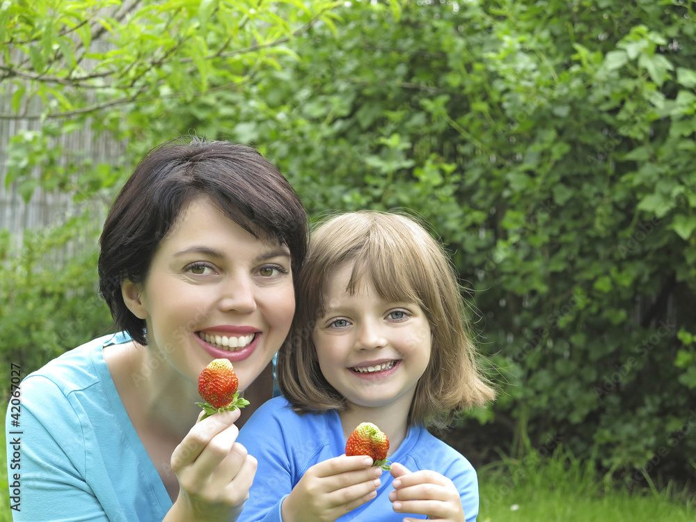 happy mother and her daughter eating strawberries in the garden happy mother and her daughter eating strawberries in the garden