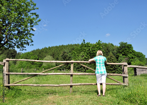 Frau am Zaun schaut auf die Wiese