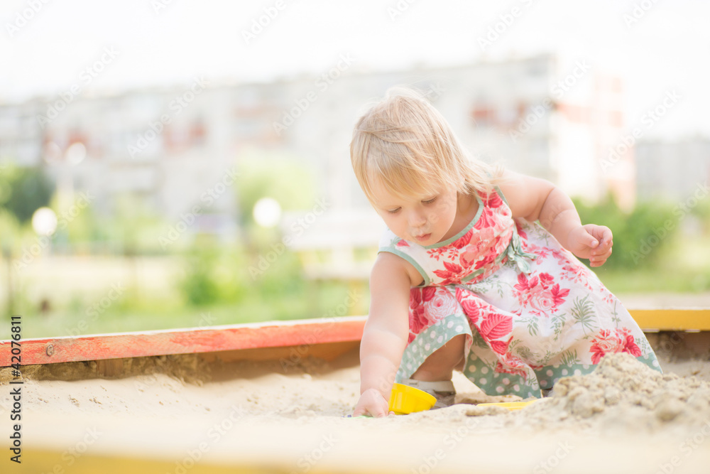 Fototapeta premium Adorable toddler girl in dress play with sand on sandbox