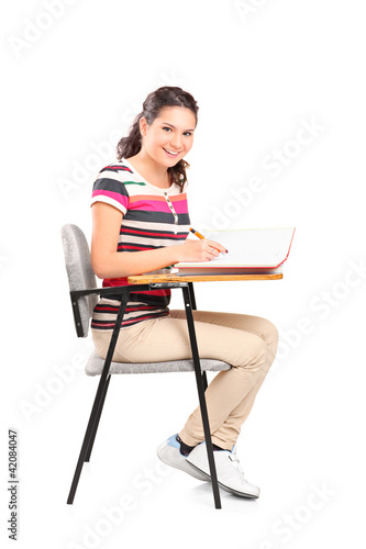 A schoolgirl sitting on a chair and writing down notes