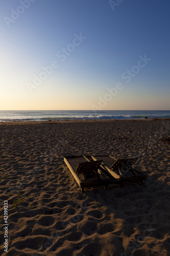 sunrise on a beach, wood beach chairs in foreground