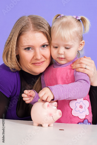 Pretty Caucasian mum with her daughter play with the piggy bank