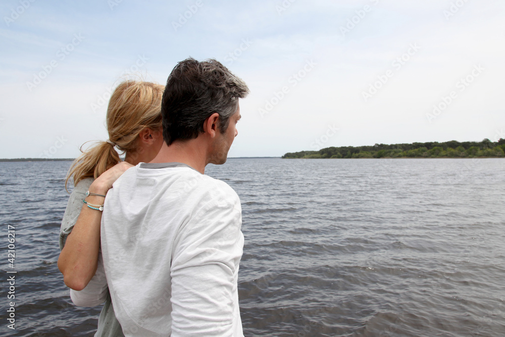 Profile view of couple sitting on a wooden bridge by a lake