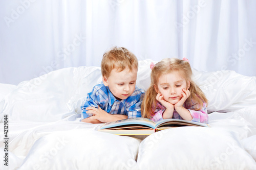 Little girl and boy read the book in the bed