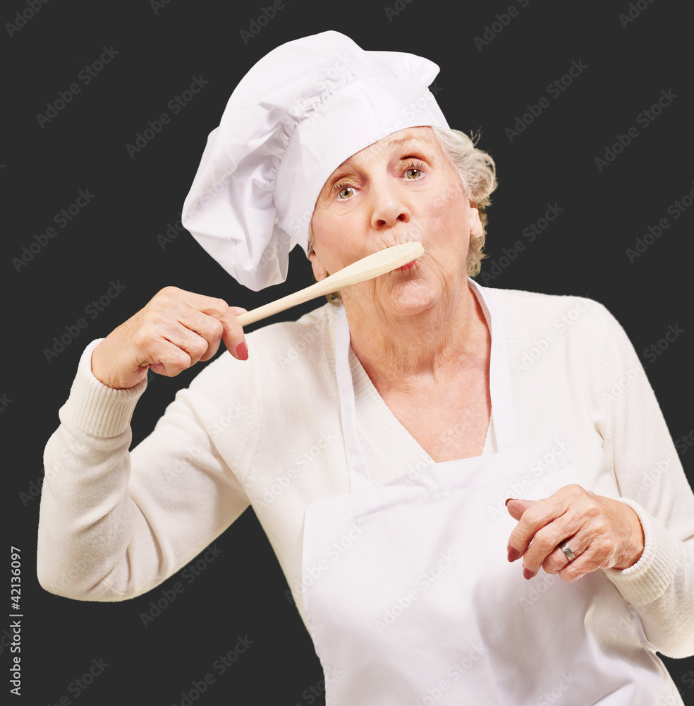 portrait of cook senior woman with wooden spoon on mouth over bl portrait of cook senior woman with wooden spoon on mouth over bl