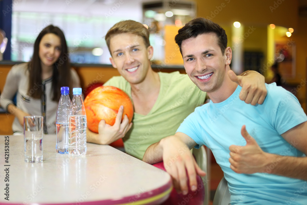 Obraz premium Two men and woman with balls sit at table in bowling