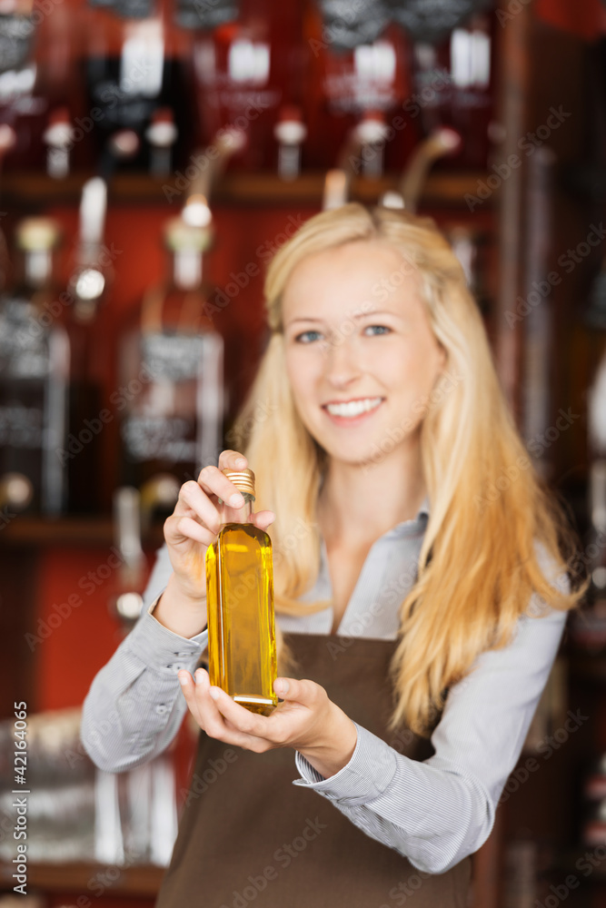 freundliche verkäuferin zeigt eine kleine flasche öl freundliche verkäuferin zeigt eine kleine flasche öl