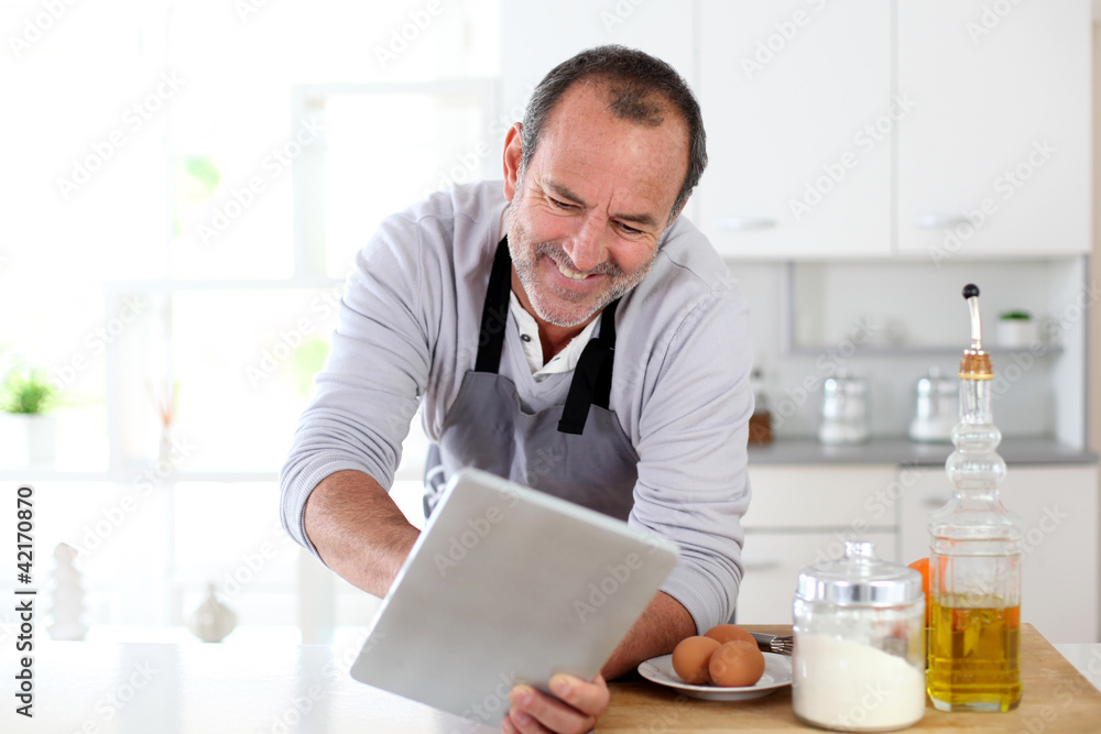 Senior man in kitchen using electronic tablet Senior man in kitchen using electronic tablet