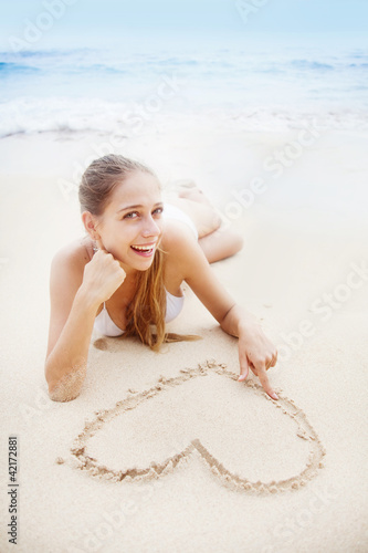 young beautiful woman on the beach making heart on the sand