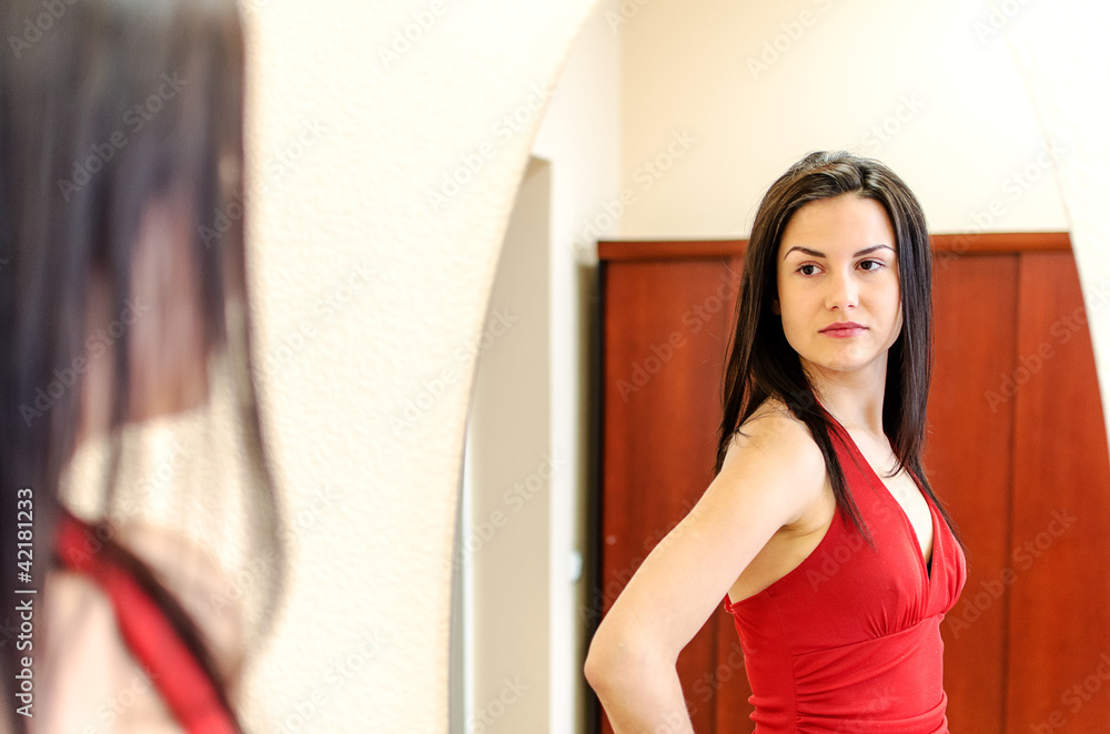 Beautiful girl in red dress posing in front of a mirror Beautiful girl in red dress posing in front of a mirror