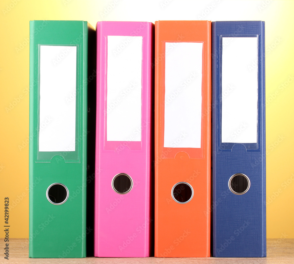 bright office folders on wooden table on yellow background. bright office folders on wooden table on yellow background.