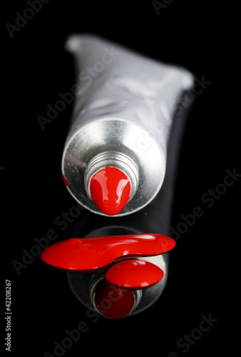 Red paint follows from the tube on black background close-up photo