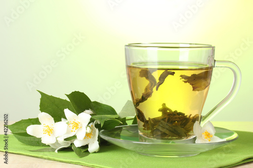 cup of green tea with jasmine on table on green background