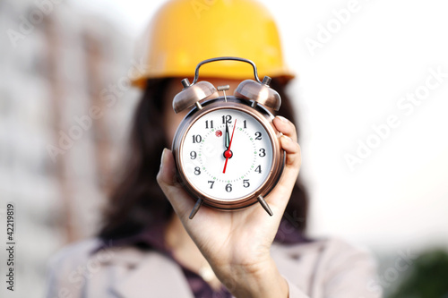 Cheerful female construction engineer holding alarm clock