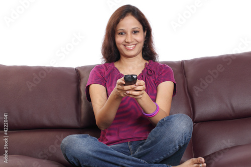 Happy Indian young woman sitting on sofa watching television