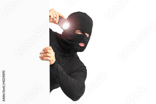 Foto A thief with robbery mask holding a flashlight behind a white pa