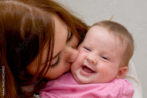 Closeup faces of young happy mother kissing newborn baby