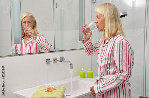 Seniorin trinkt im Badezimmer ein Glas Wasser photo