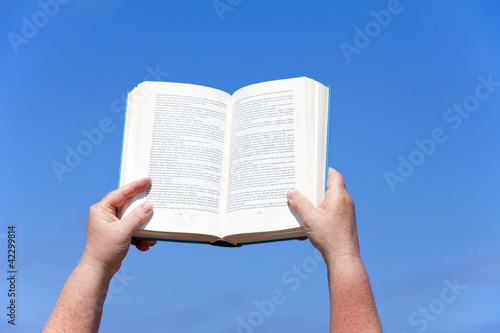 Hände halten ein Buch gegen den blauen Himmel