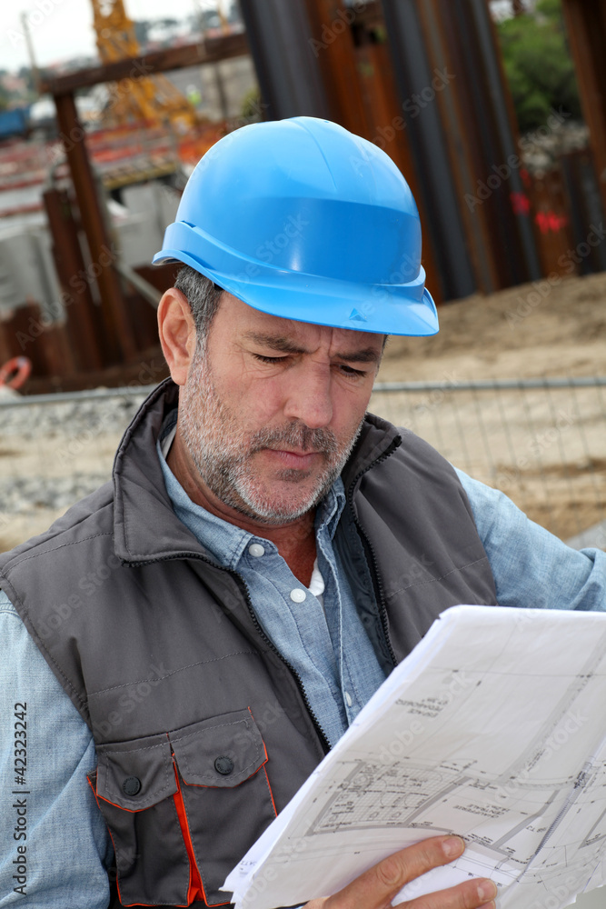Construction manager controlling building site with plan Construction manager controlling building site with plan