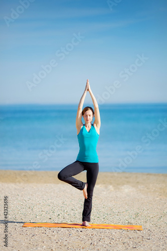 Young woman meditating on the beach .