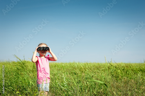 Little girl in field looking away through binoculars at you