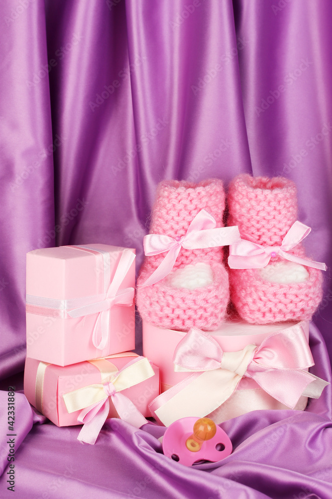 pink baby boots, pacifier, gifts on silk background. pink baby boots, pacifier, gifts on silk background.
