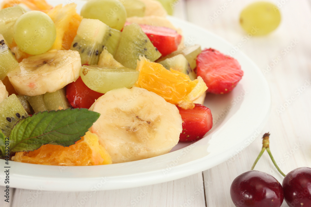 Fresh fruits salad on plate and berries on white wooden table Fresh fruits salad on plate and berries on white wooden table