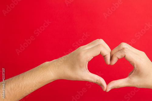 Hands in the shape of heart isolated on red background