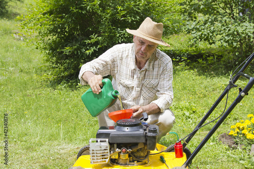 Mid age man adding oil to lawn mover in the garden