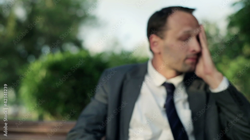 Depressed, sad young businessman sitting in the park Depressed, sad young businessman sitting in the park