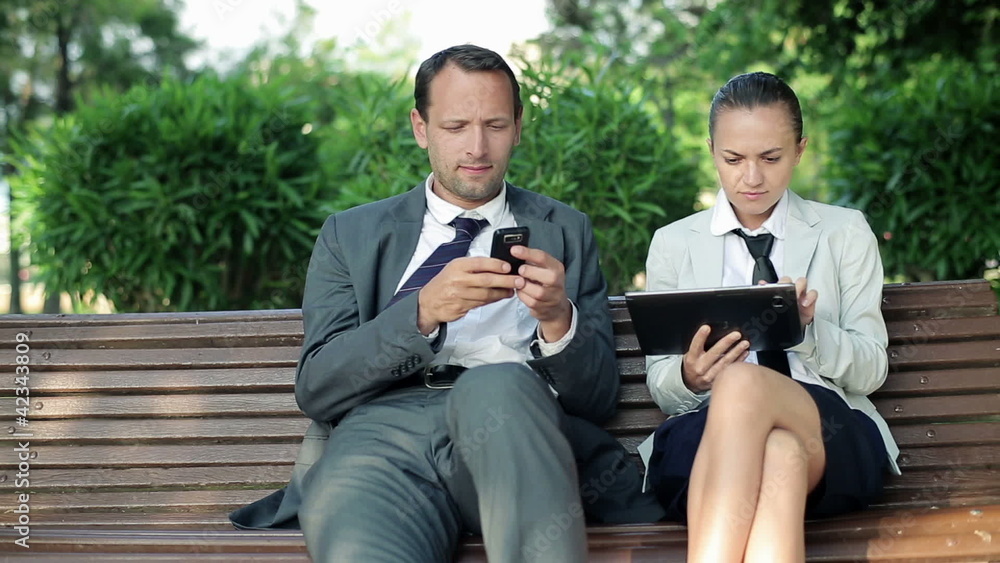 Business couple with tablet and cellphone in park, dolly shot Business couple with tablet and cellphone in park, dolly shot