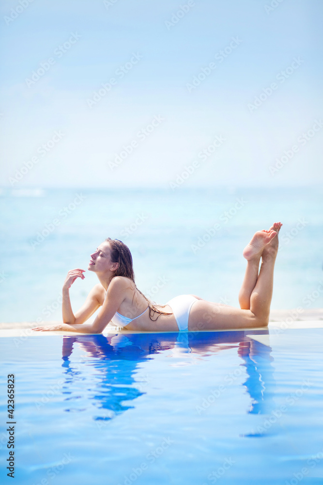 Young beautiful woman sitting on the side of swimming pool, bali