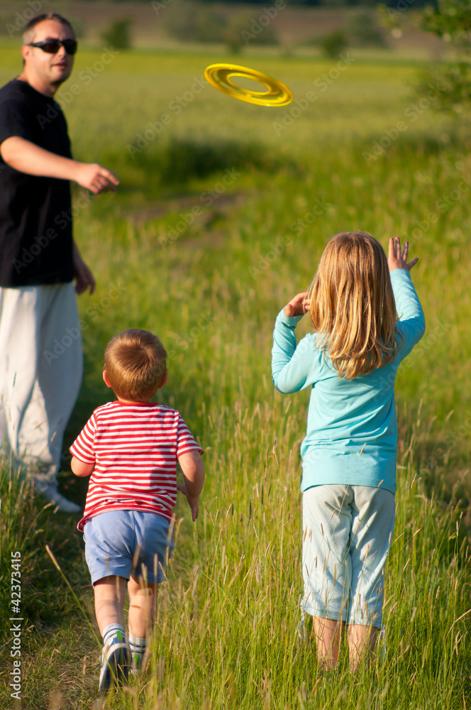 Fototapeta premium Father and his children play with frisbee on sunny spring day