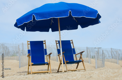 Blue beach umbrella and two matching chairs at the seashore