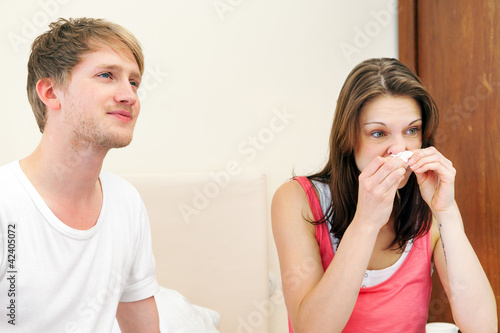 Frau putzt sich Nase neben Mann im Bett